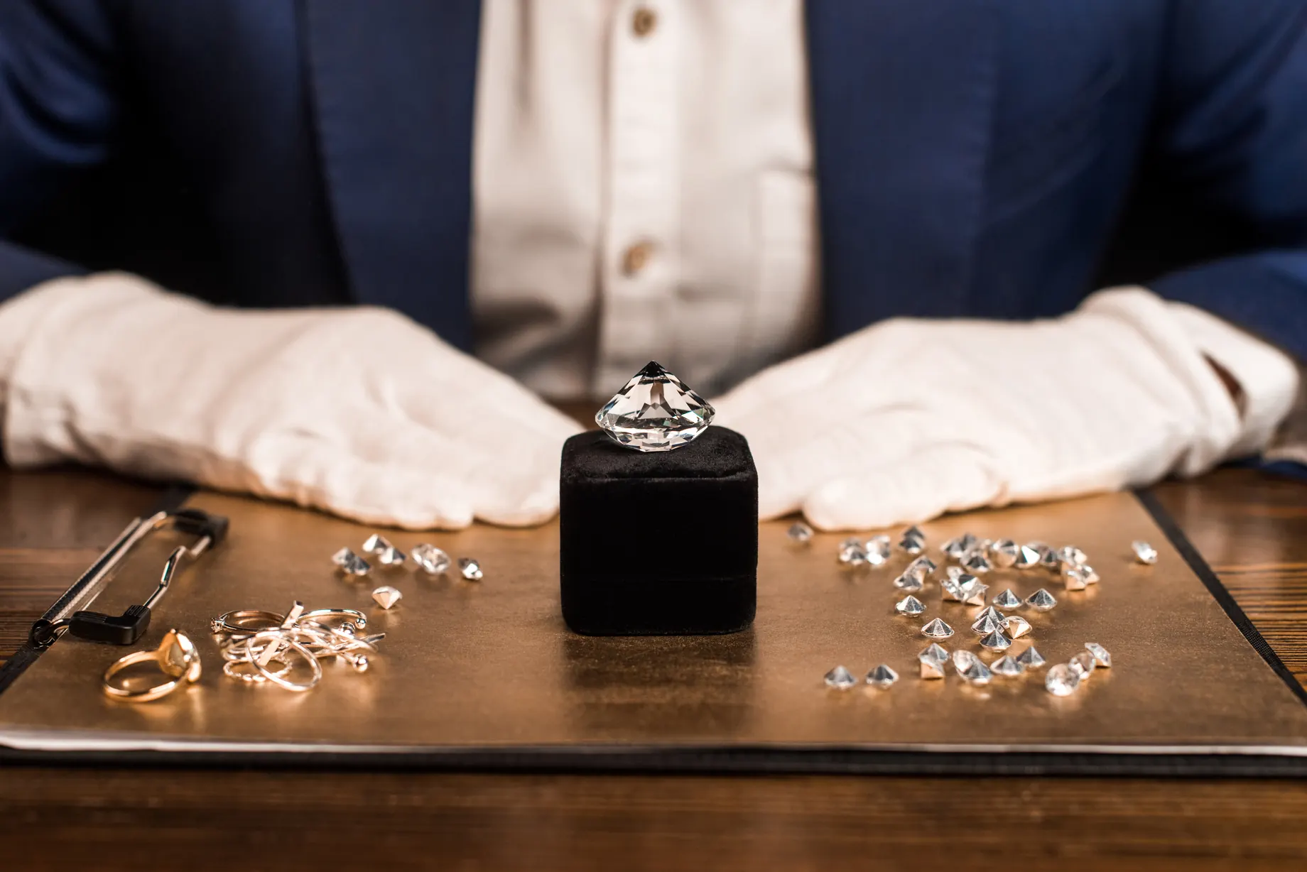 Gloved hands presenting a polished diamond and a small parcel of stones